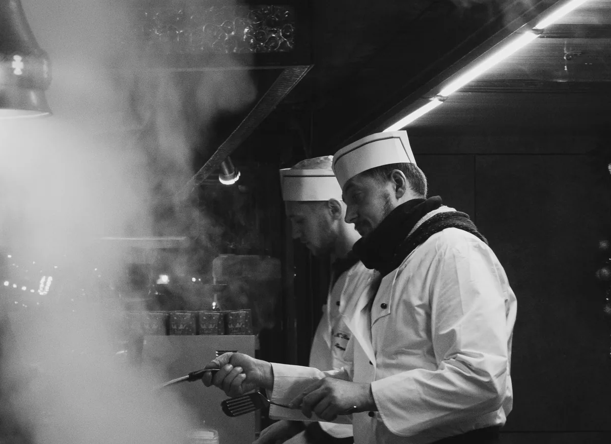 A chef in whites and a toque working through the steam of the pass