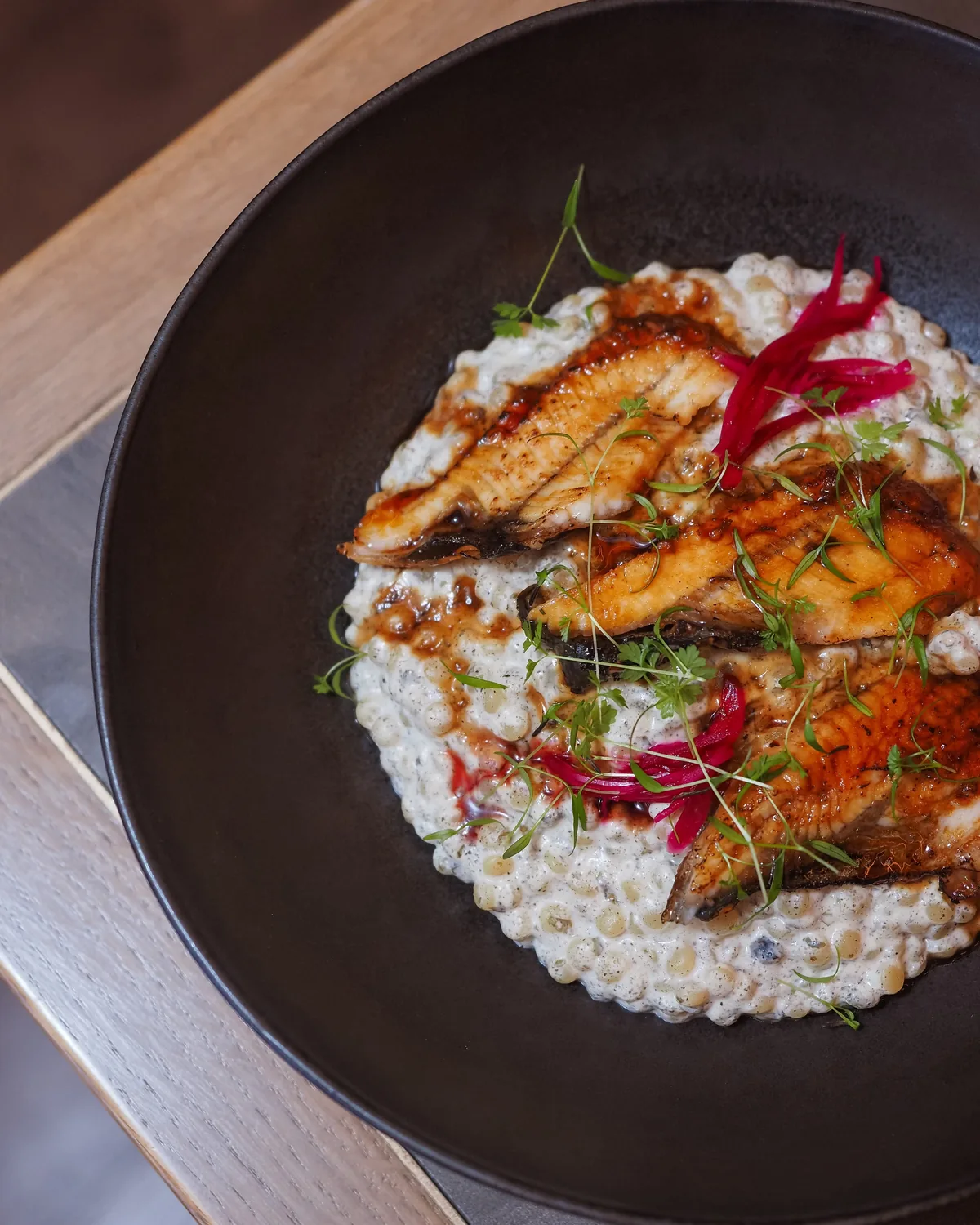 Line-caught bass on a creamy spelt risotto, served in a dark stoneware bowl