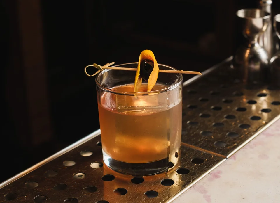 An Old Fashioned with an orange twist on a dark bar counter