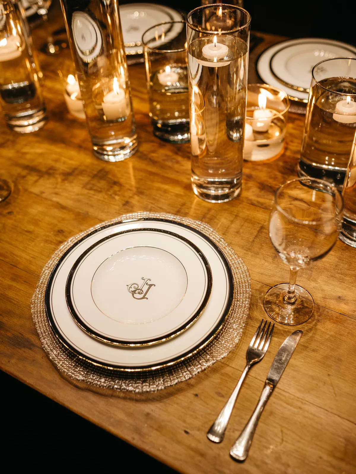 A candlelit table laid with monogrammed plates and crystal glasses